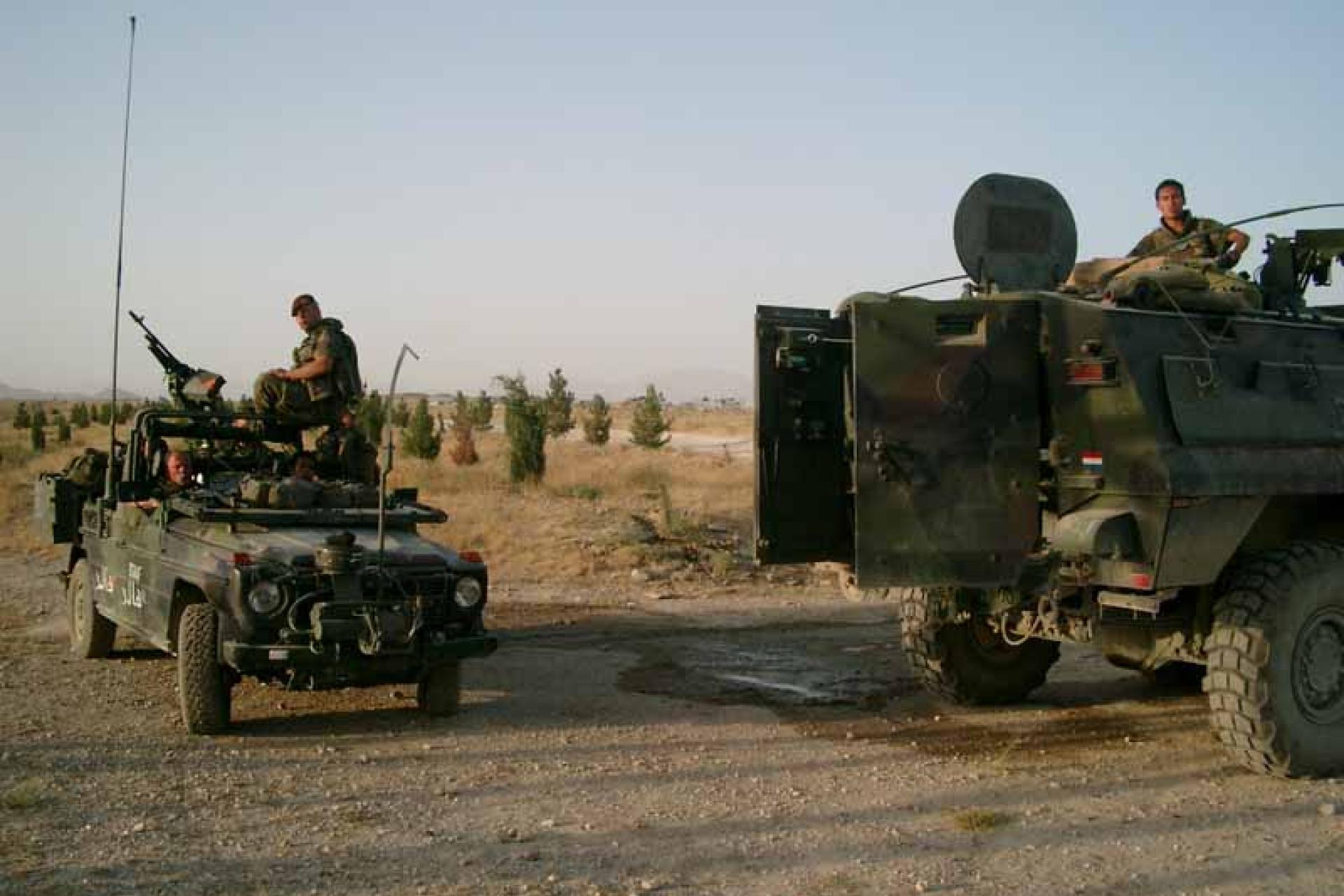 Militaire voertuigen met soldaten staan op een zandweg