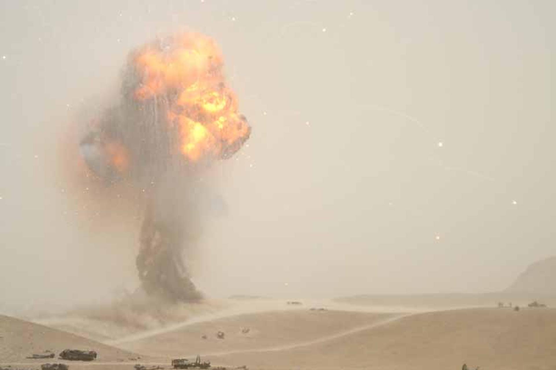 Vergroot afbeelding woestijn met op de achtergrond een ontploffing met vuur en rookwolk
