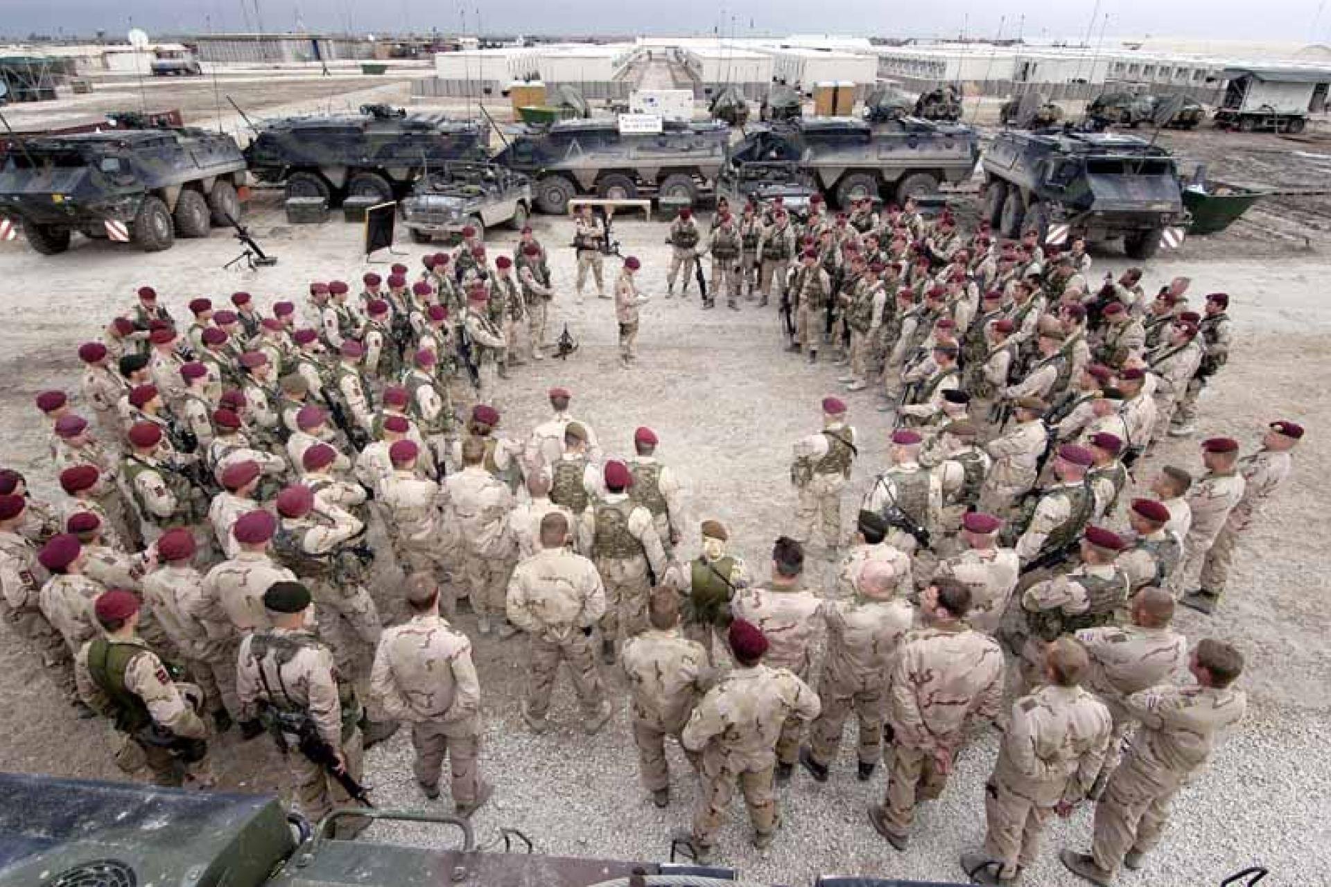Vergroot afbeelding Militairen met rode baretten staan rondom opgesteld, op de achtergrond staan militaire voertuigen