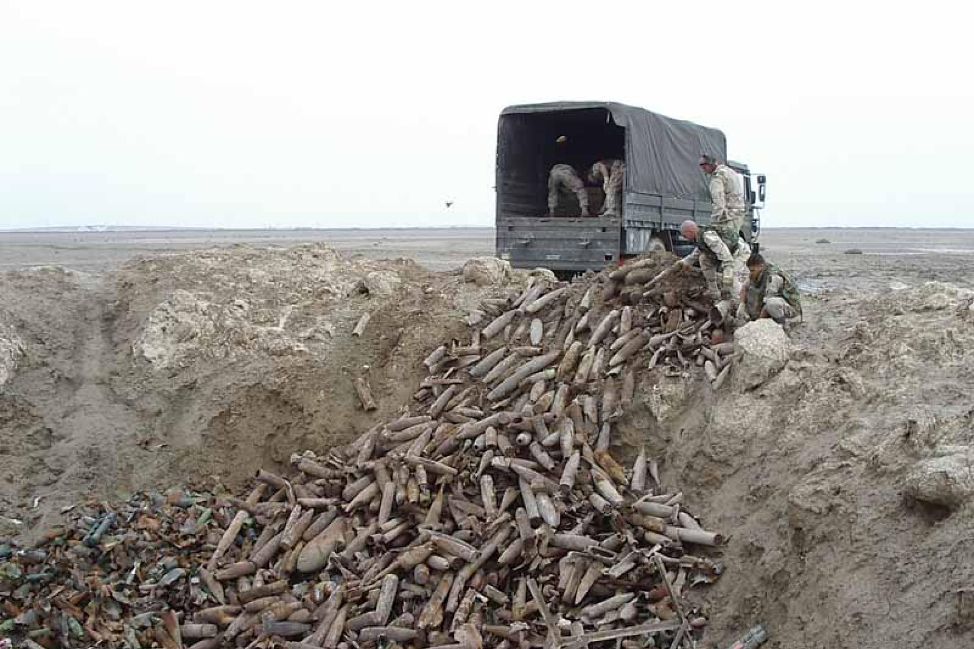 Militaire truck en soldaten die  oude munitie dumpen in een gat in het zand