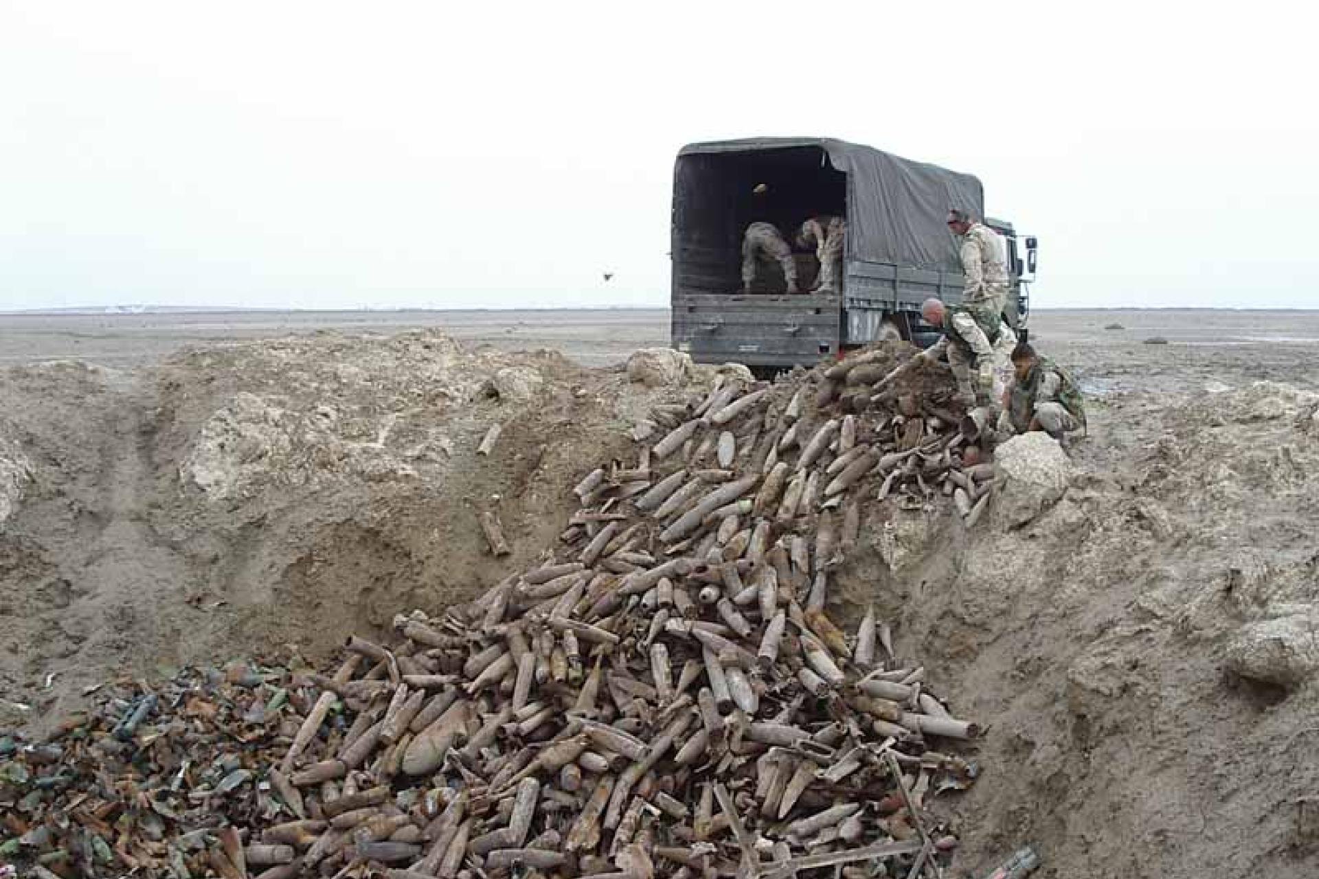 Vergroot afbeelding Militaire truck en soldaten die  oude munitie dumpen in een gat in het zand