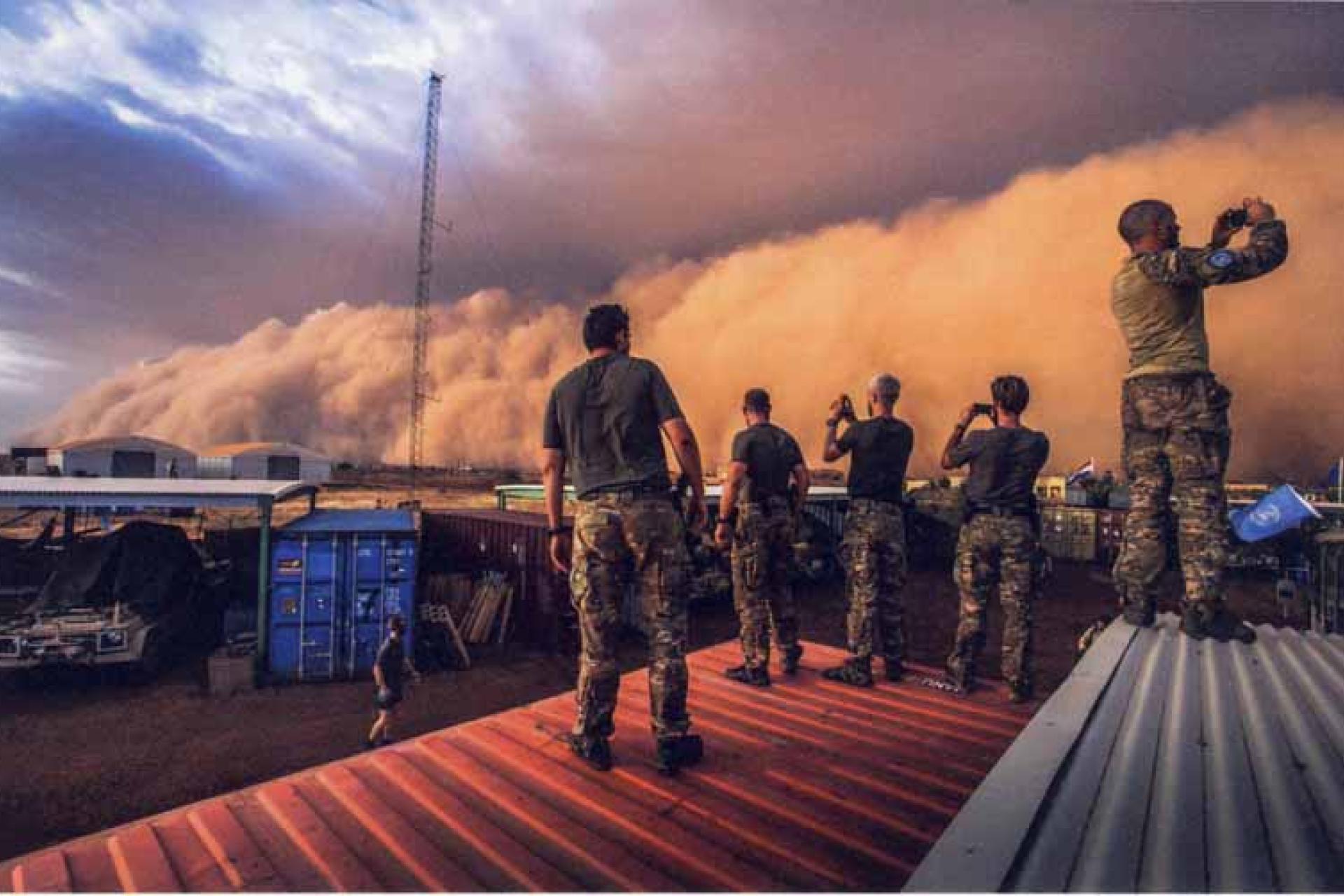 Militairen die bovenop een container staan en foto's maken van een naderende zandstorm