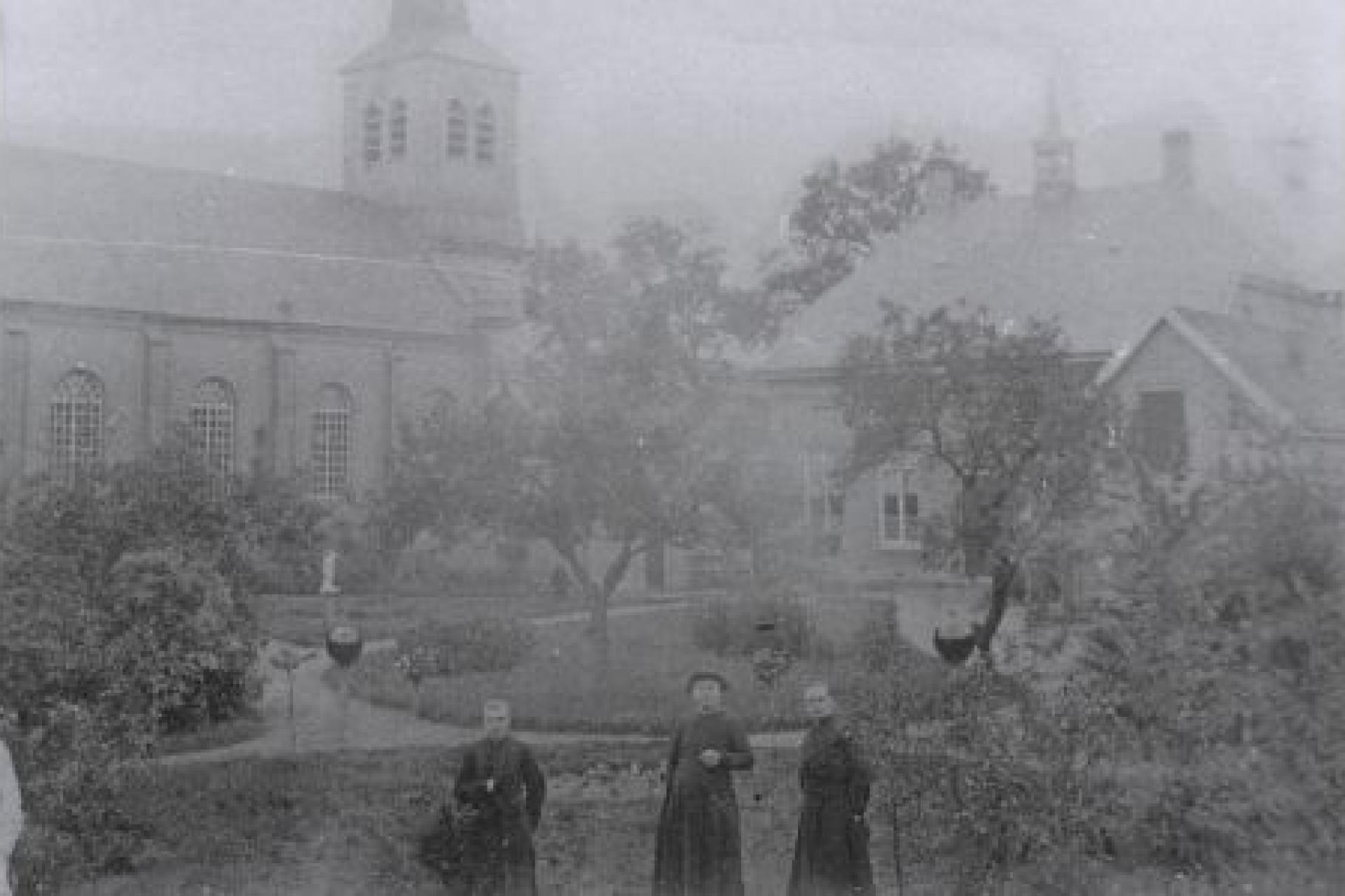 oude foto van De Mortel met daarop 3 mannen met op de achtergrond een tuin en een kerk