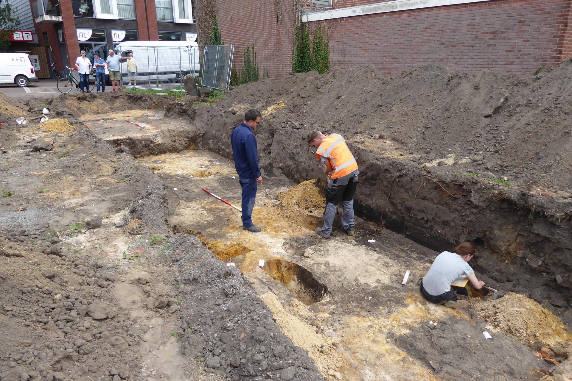 Drie mannen doen archeologisch onderzoek in een afgegraven stuk van een straat